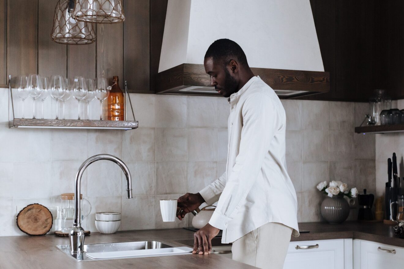 A man filling a cup with tap water in a kitchen