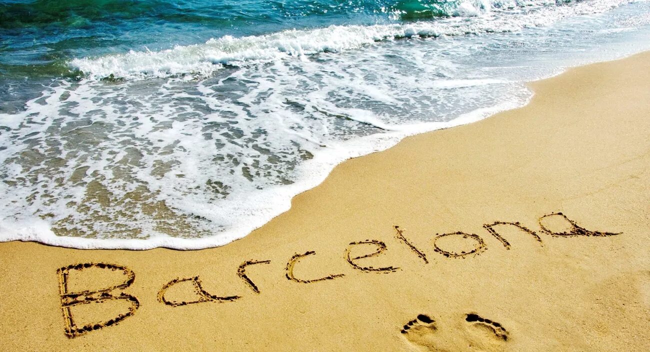 Надпись Barcelona на мокром песке у кромки воды
